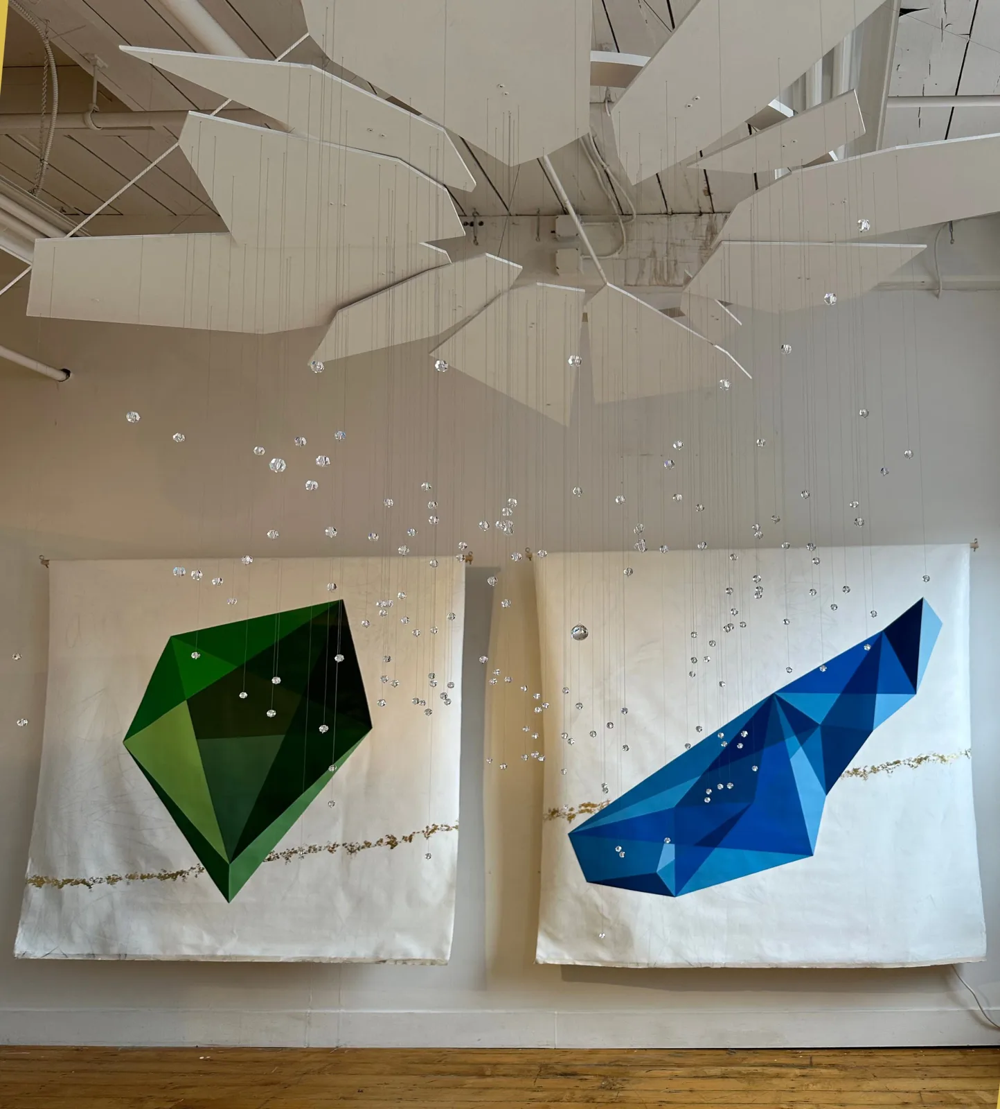 Suspended geometric sculpture with green and blue faceted forms, descending spheres, and articulated ceiling element.
