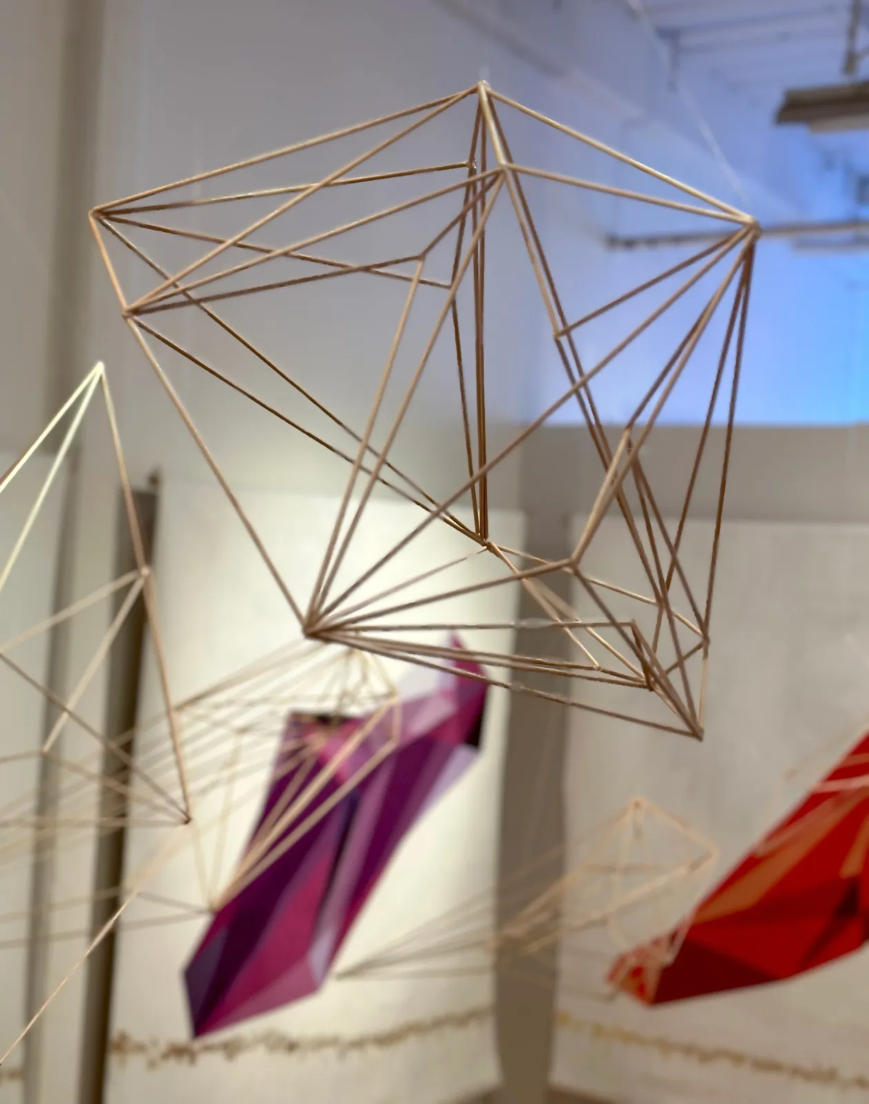 A bronze or copper wireframe geometric sculpture casting intricate light shadows on surrounding surfaces.