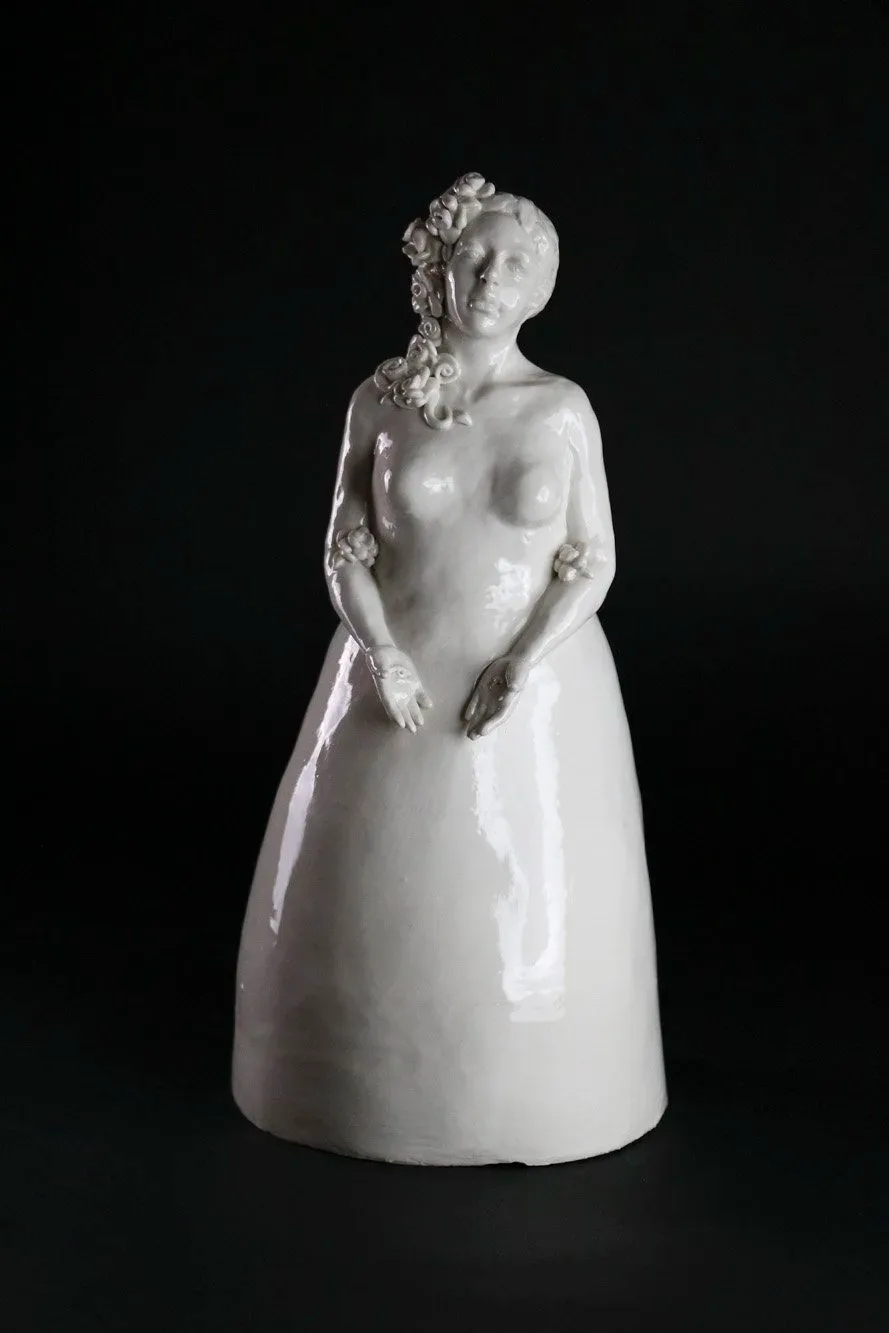 A white glazed ceramic sculpture depicting a female torso with floral hair ornaments and draped lower form.
