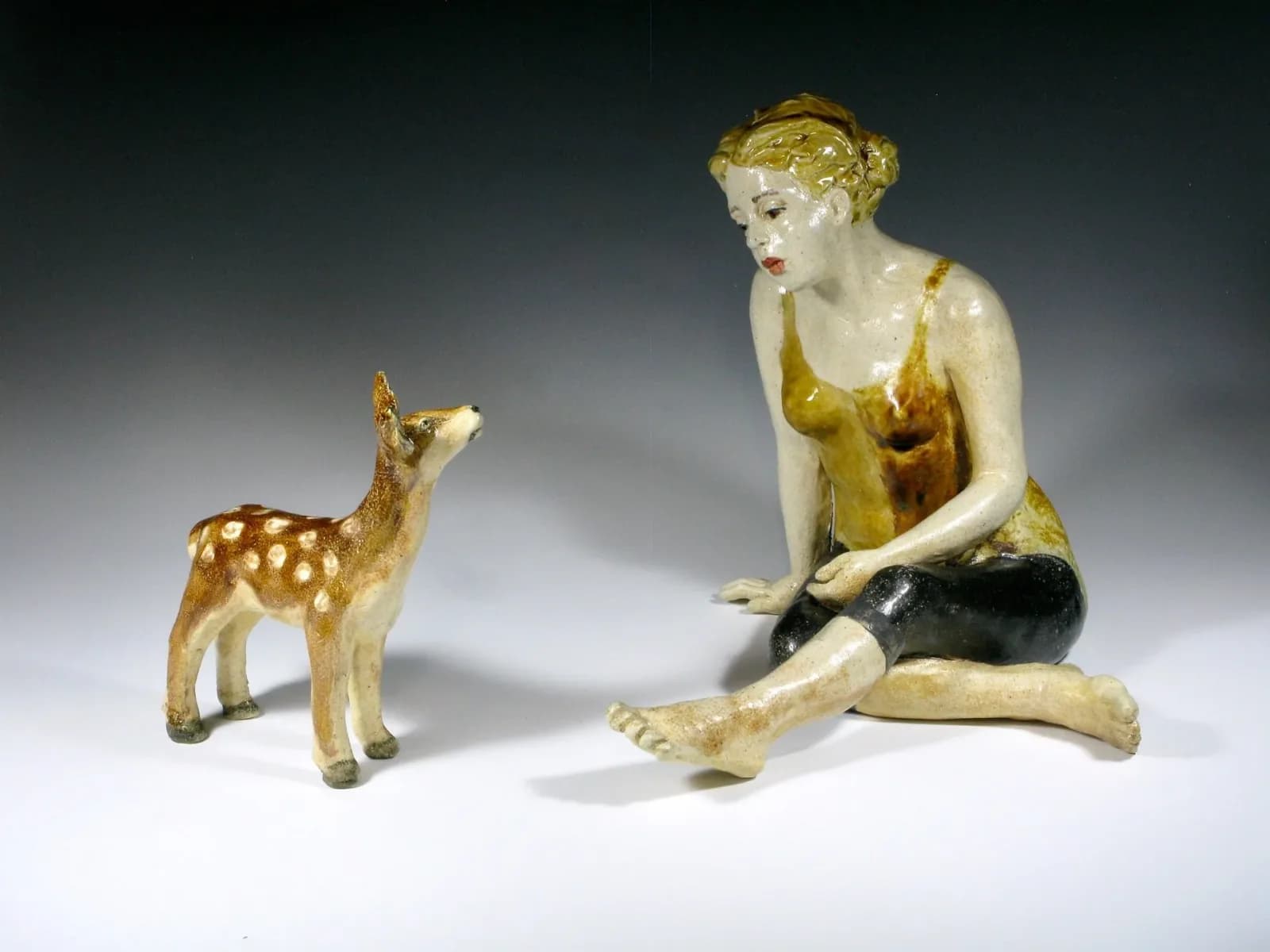 Seated woman and spotted fawn rendered in polychromed and gilded ceramic, a figurative sculptural composition.