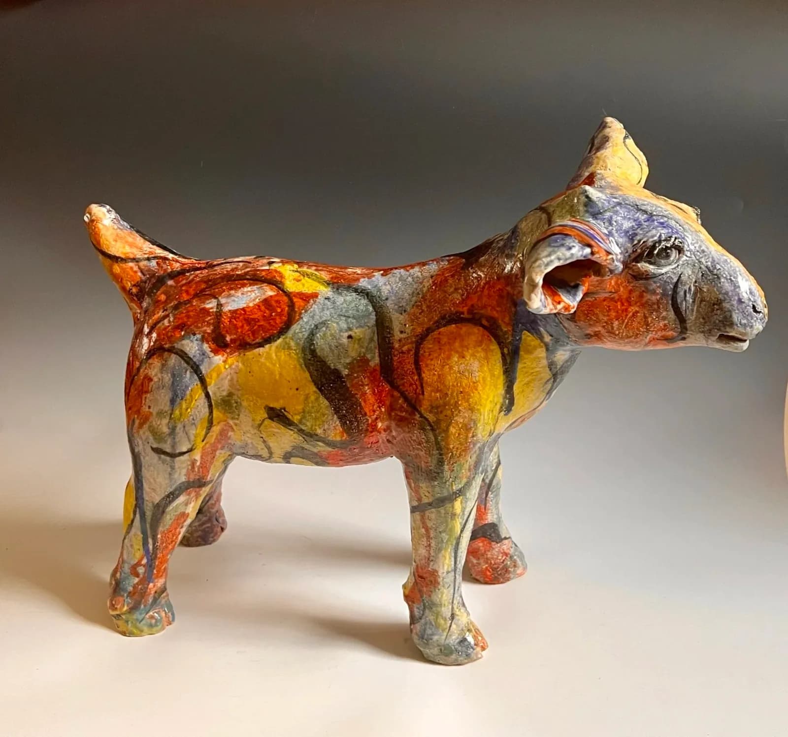 Hand-painted ceramic cow sculpture with bold red, yellow, and orange geometric patterns throughout.