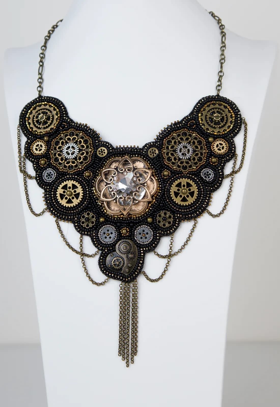 Ornate steampunk statement necklace featuring brass gears, black beading, and crystal center stone on chain.