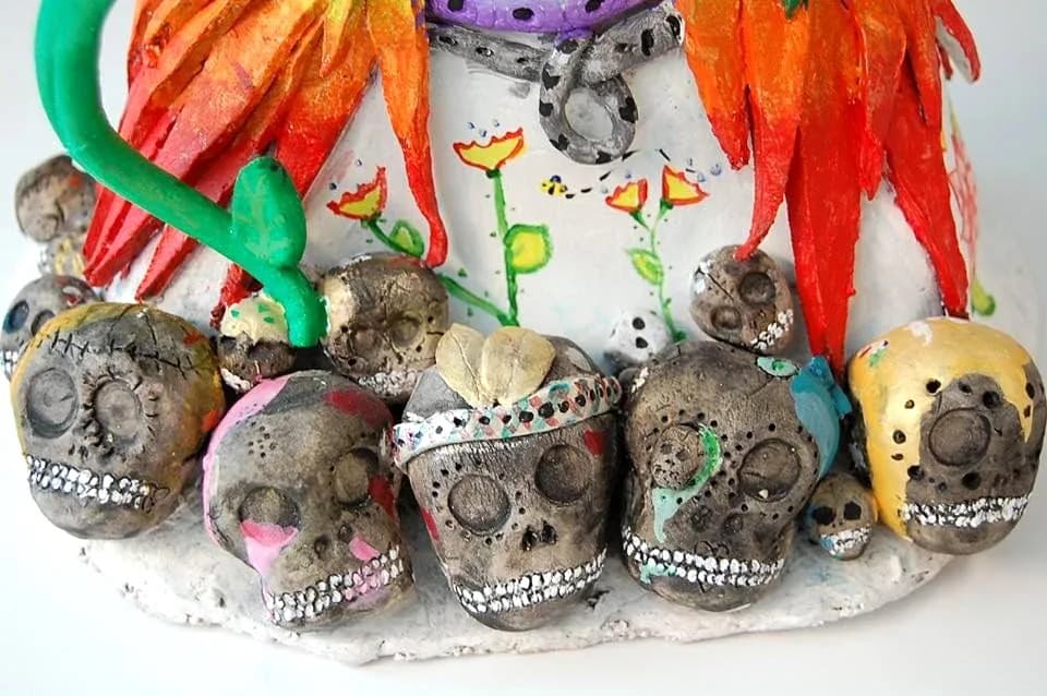 Clay skulls decorated with silver, flowers, and colorful adornments in folk art assemblage.