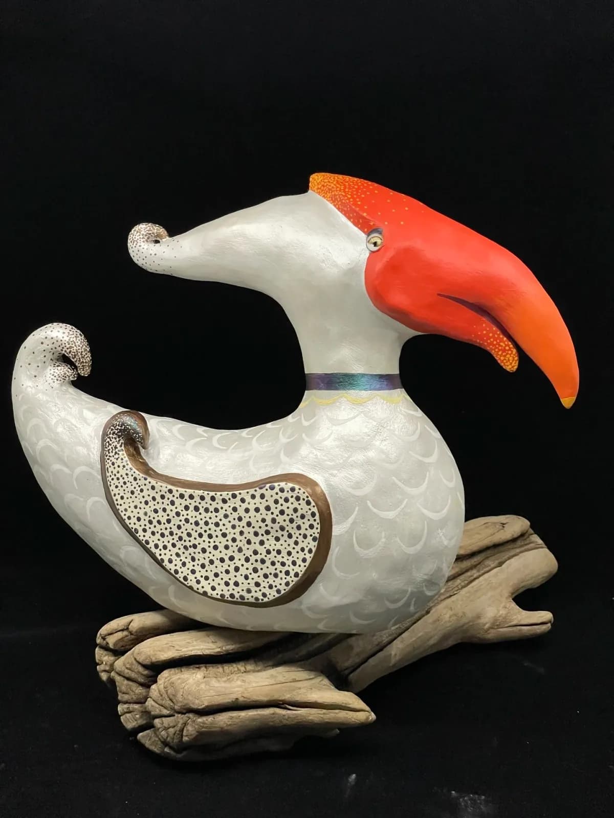 Hand-carved wooden bird sculpture with white body, red crest, and wood-branch feet against black background.