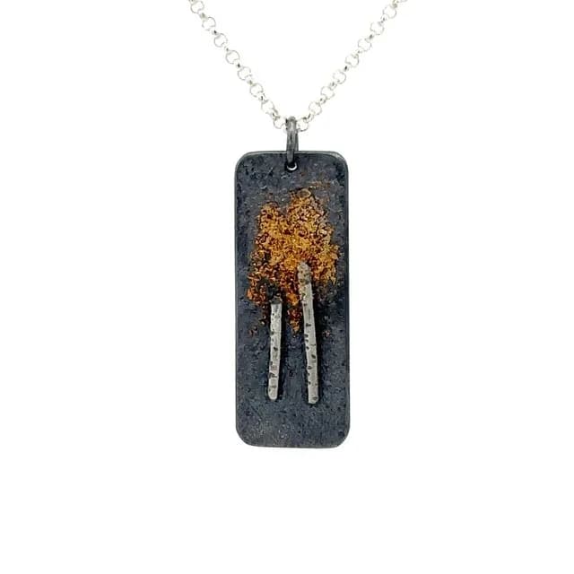 Oxidized metal pendant featuring a gold-leaf tree on silver chain.