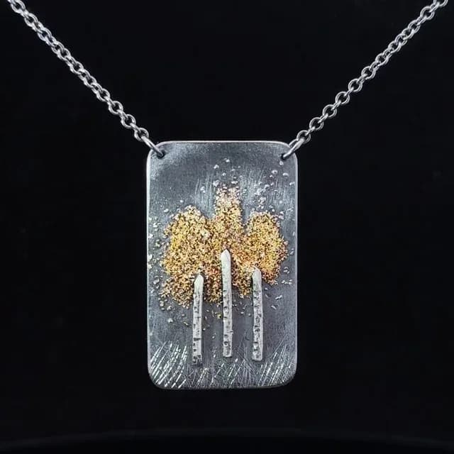 Metalsmith pendant necklace featuring etched silver rectangle with gold leaf tree forms and chain.