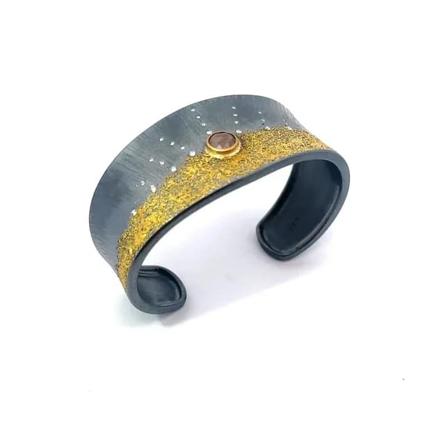Mixed-metal cuff bracelet with gold textured surface, oxidized silver band, and inset gemstone.