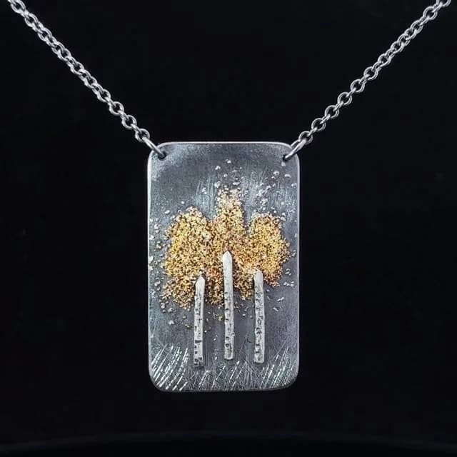 Mixed-metal pendant necklace featuring stylized aspen trees with gold-textured foliage on a silver rectangular face.