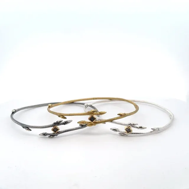 Hand-forged mixed-metal bangles in brass and silver with organic branch-like forms and stone accents.