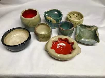 Grouping of handthrown ceramic bowls and vessels in muted earth tones and glazed greens, arranged on white.