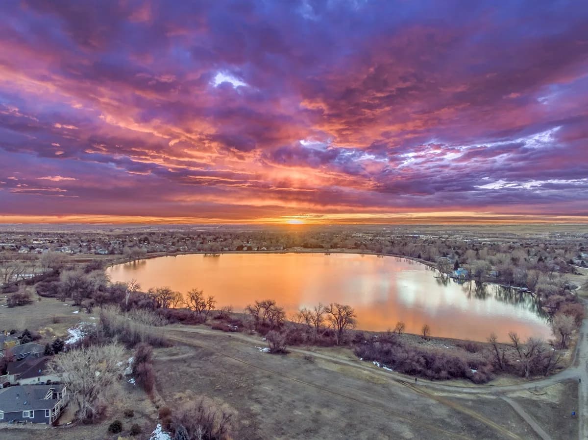 Aerial photograph of a lake at sunset with dramatic purple and orange sky reflected in the water below.
