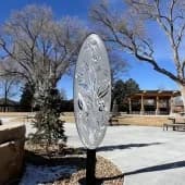 Abstract stone sculpture with a large circular opening, sited in an open plaza.