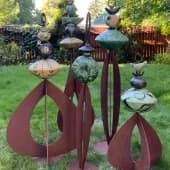 Metal sculptural flowers with ceramic or painted accents in a lawn garden setting.