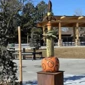 Abstract wooden sculpture with warm carved spiral form displayed outdoors on a stone base.