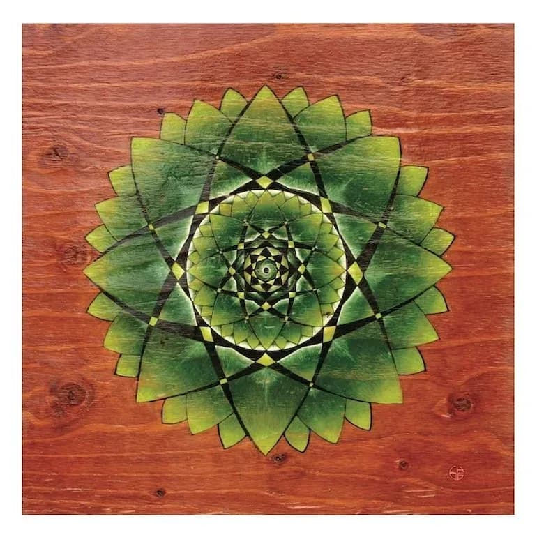 A geometric mandala with radiating green petals and nested diamond patterns on a warm wood surface.