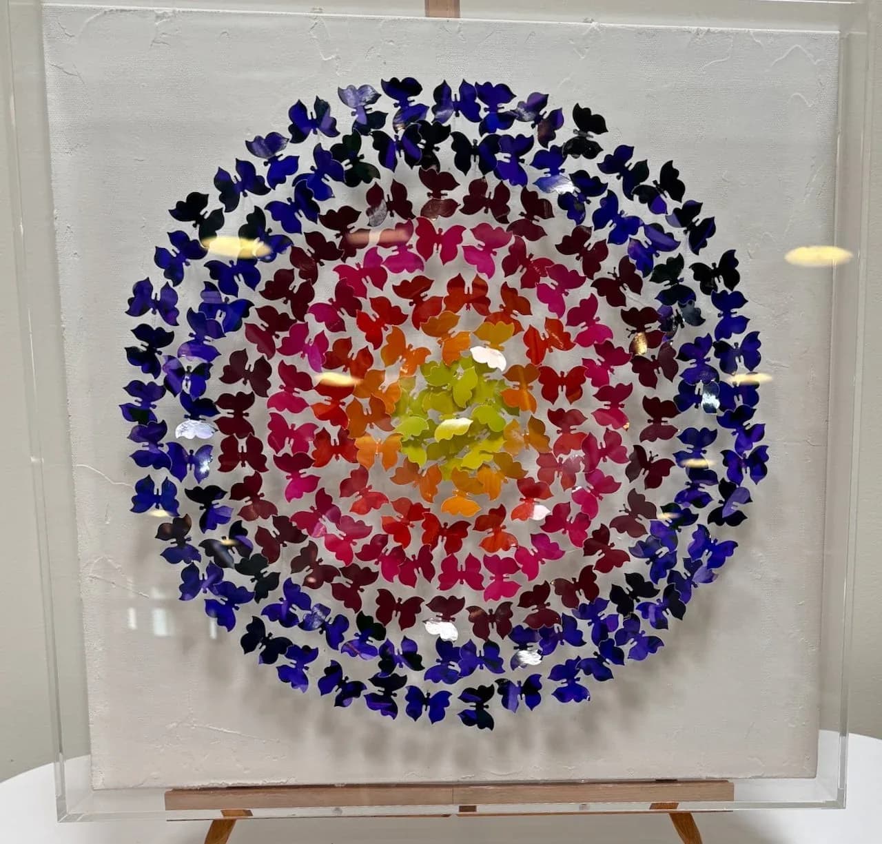 A radial mandala composed of hundreds of colorful paper butterfly cutouts arranged in concentric rings.