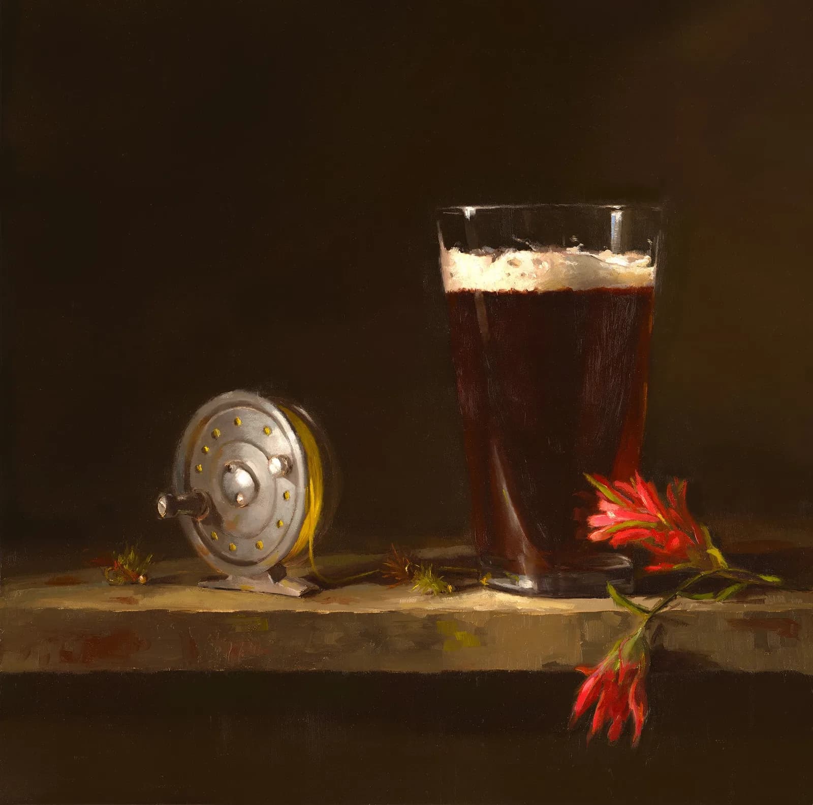 Vintage fishing reel, pint glass, and red flowers arranged on a wooden surface.