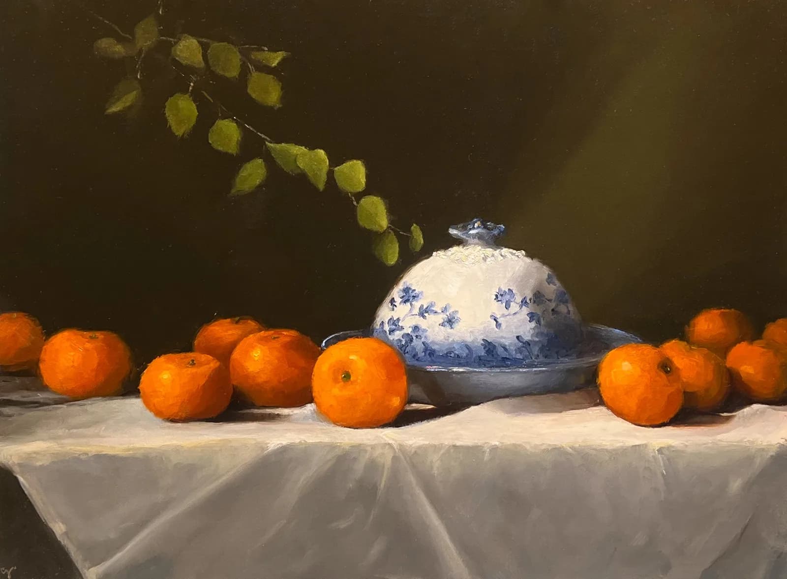Still life with oranges, blue-and-white ceramic dome, and birch leaves on draped cloth.