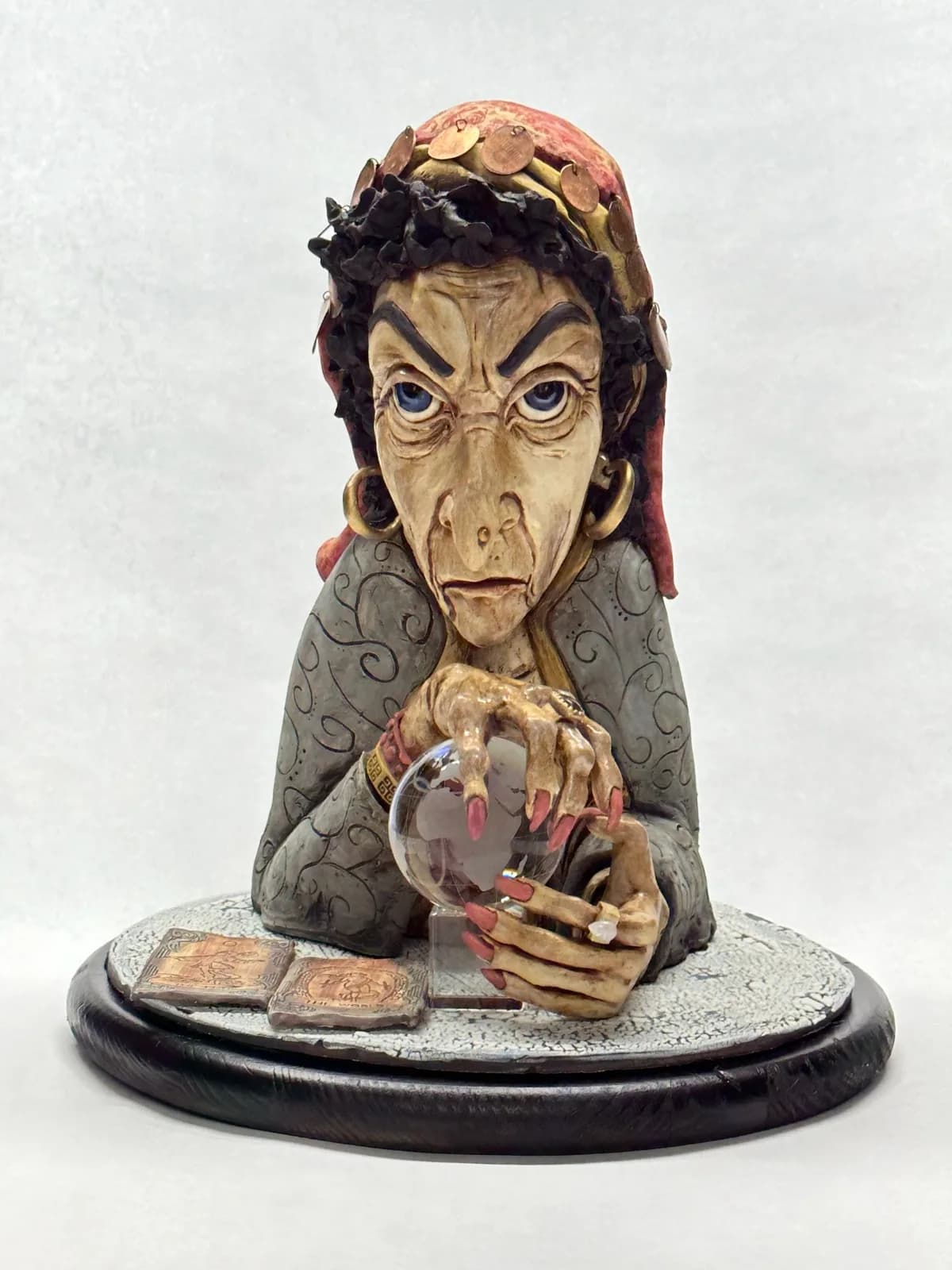 Ceramic sculpture of a witch-like figure holding a crystal sphere, mounted on a dark base.