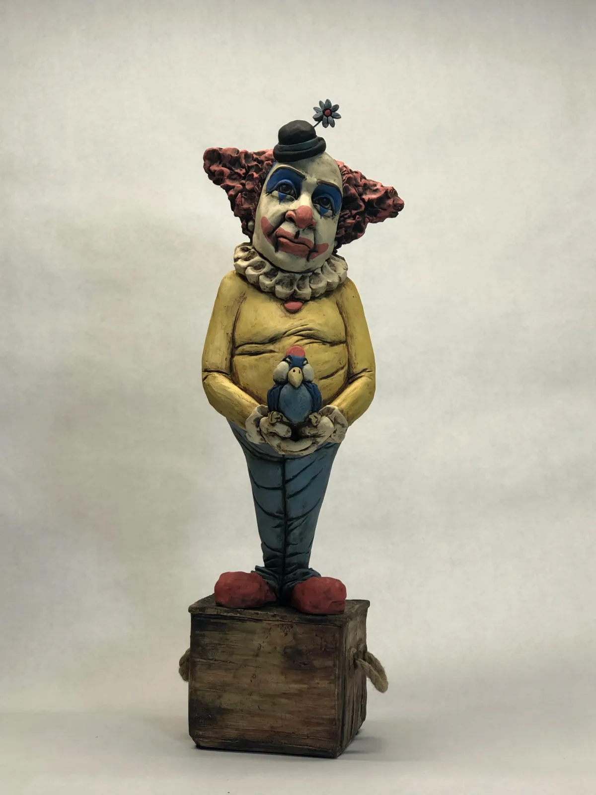 Whimsical carved wooden clown figure with painted details, holding a bird and wearing a small hat.