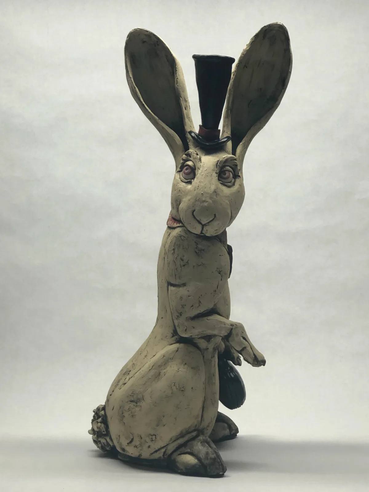 Ceramic rabbit figurine wearing a black top hat, with stylized features and weathered surface.