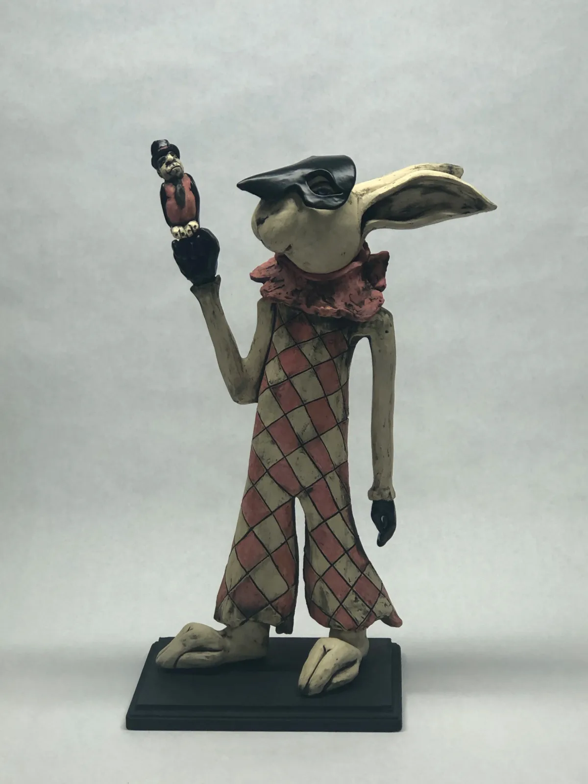 Ceramic figurative sculpture of an anthropomorphic bird character wearing a stylized outfit and holding a small perched bird.