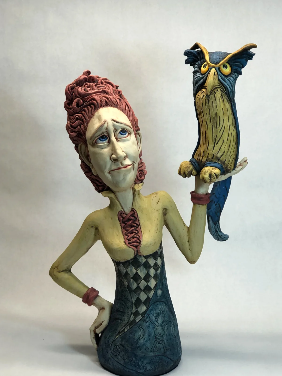 A painted ceramic bust of a woman with burgundy curled hair holding a stylized owl figure.