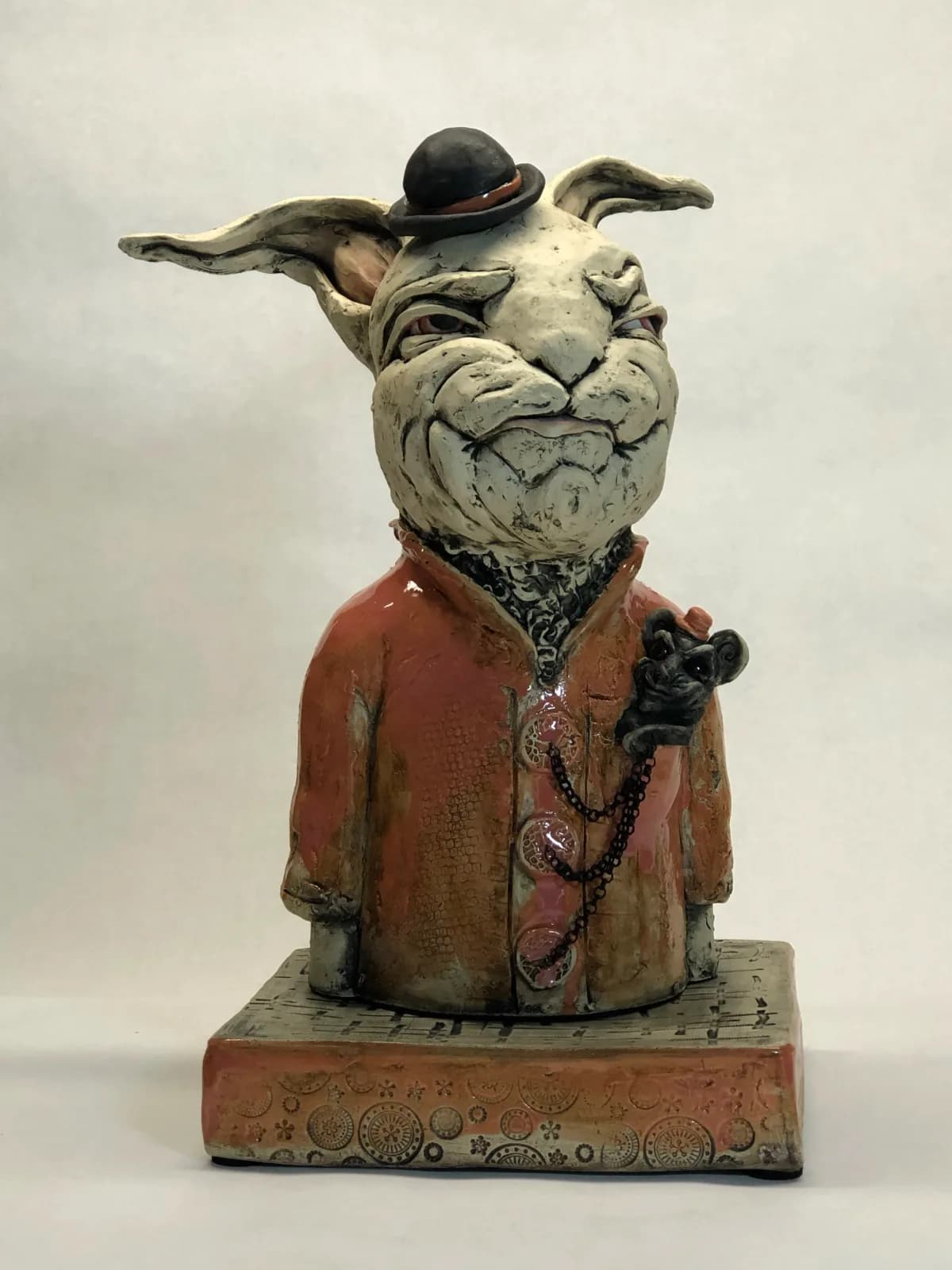 A ceramic sculptural figure of an anthropomorphic toad wearing a bowler hat and red coat, with extended arms and a small monkey companion.