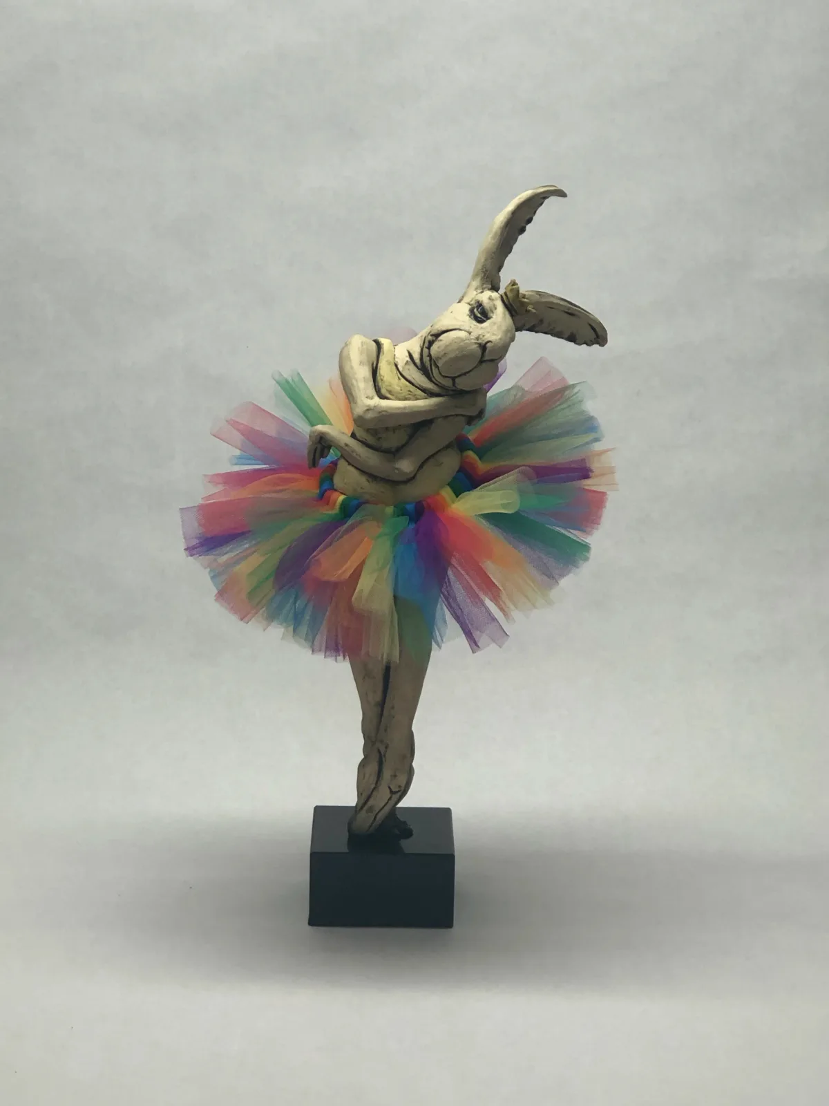 A bronze elephant figure in a colorful rainbow tutu performs a ballet pose on a black base.