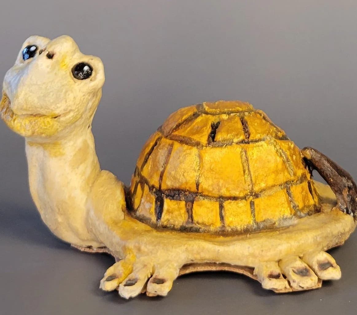 Hand-sculpted ceramic turtle with yellow glaze and black shell details, shown in three-quarter view.