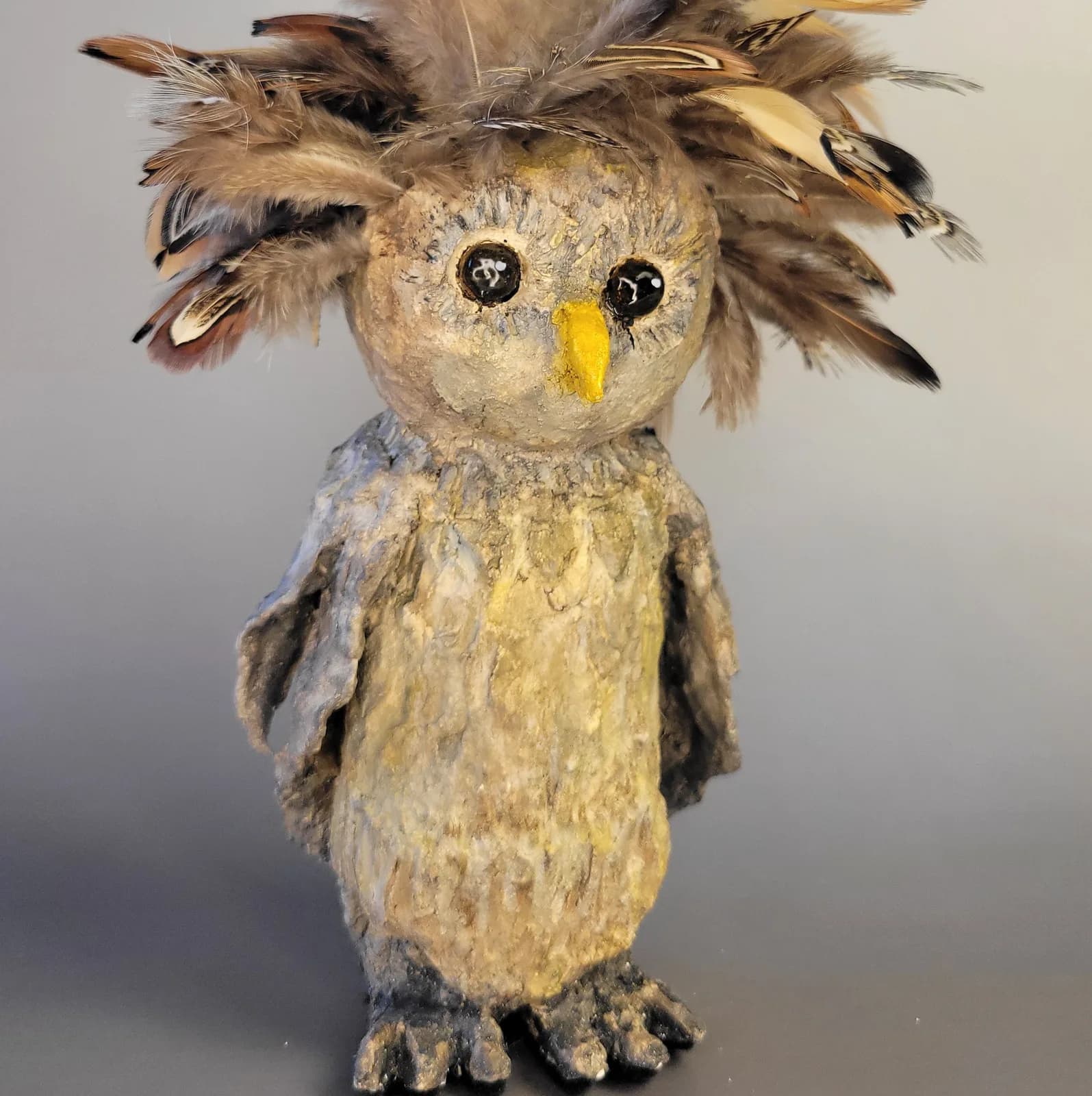 A whimsical handmade owl sculpture with natural feathers and painted facial features.