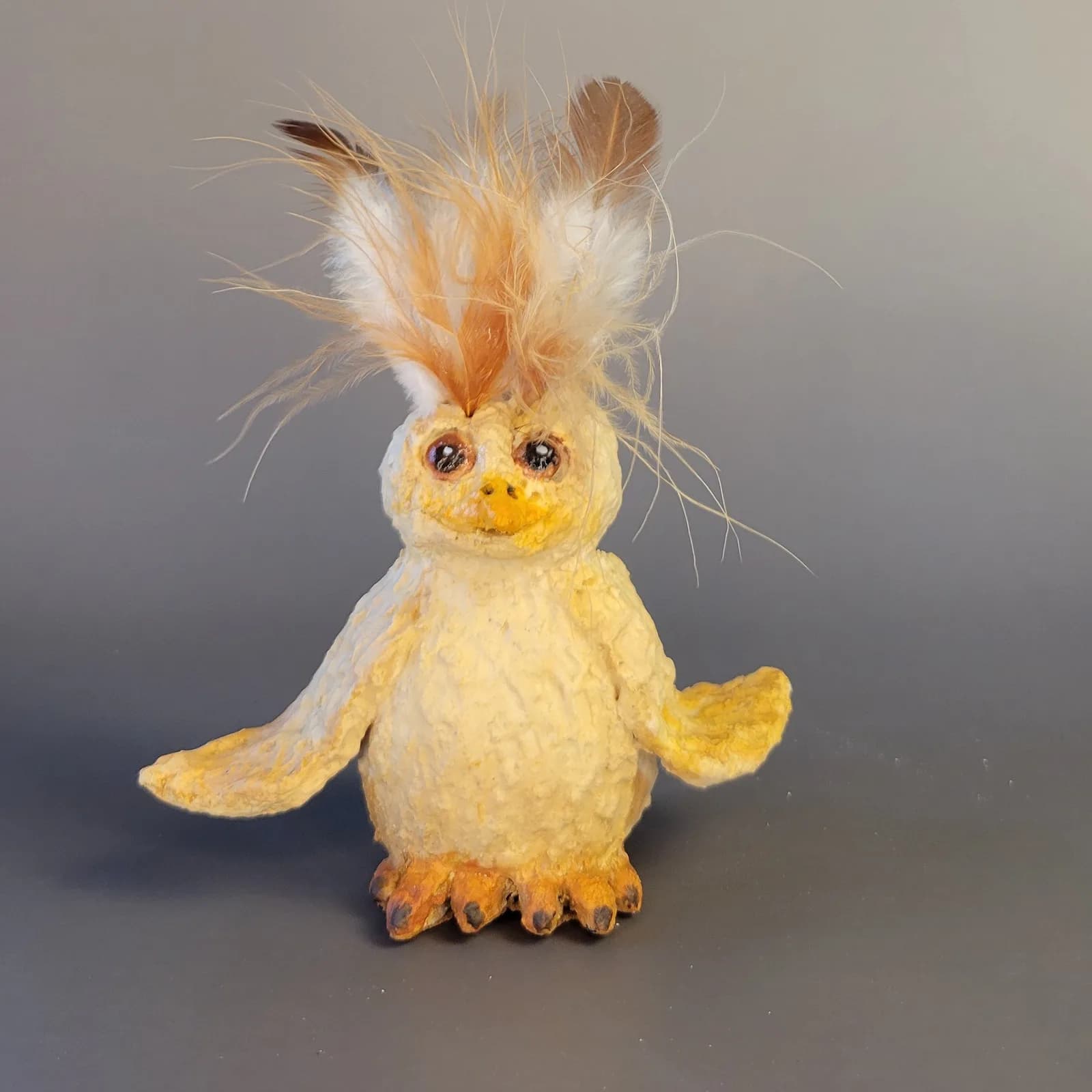 Whimsical felted and fiber bird sculpture with cream body, orange accents, and wispy feathered crown.