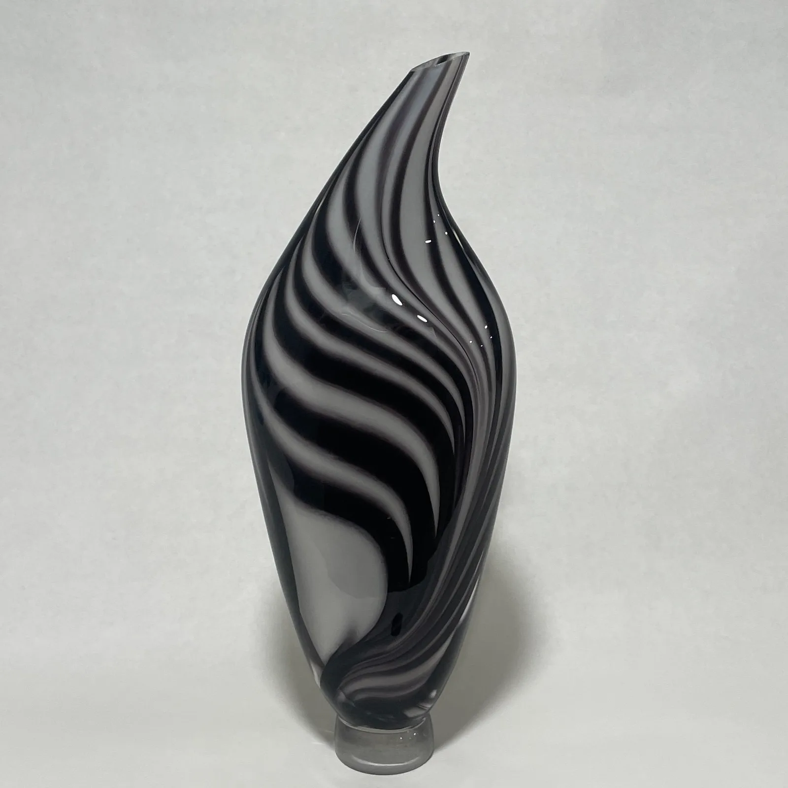 A fluid glass sculpture with twisted black and white striped patterns suggests a rising flame.