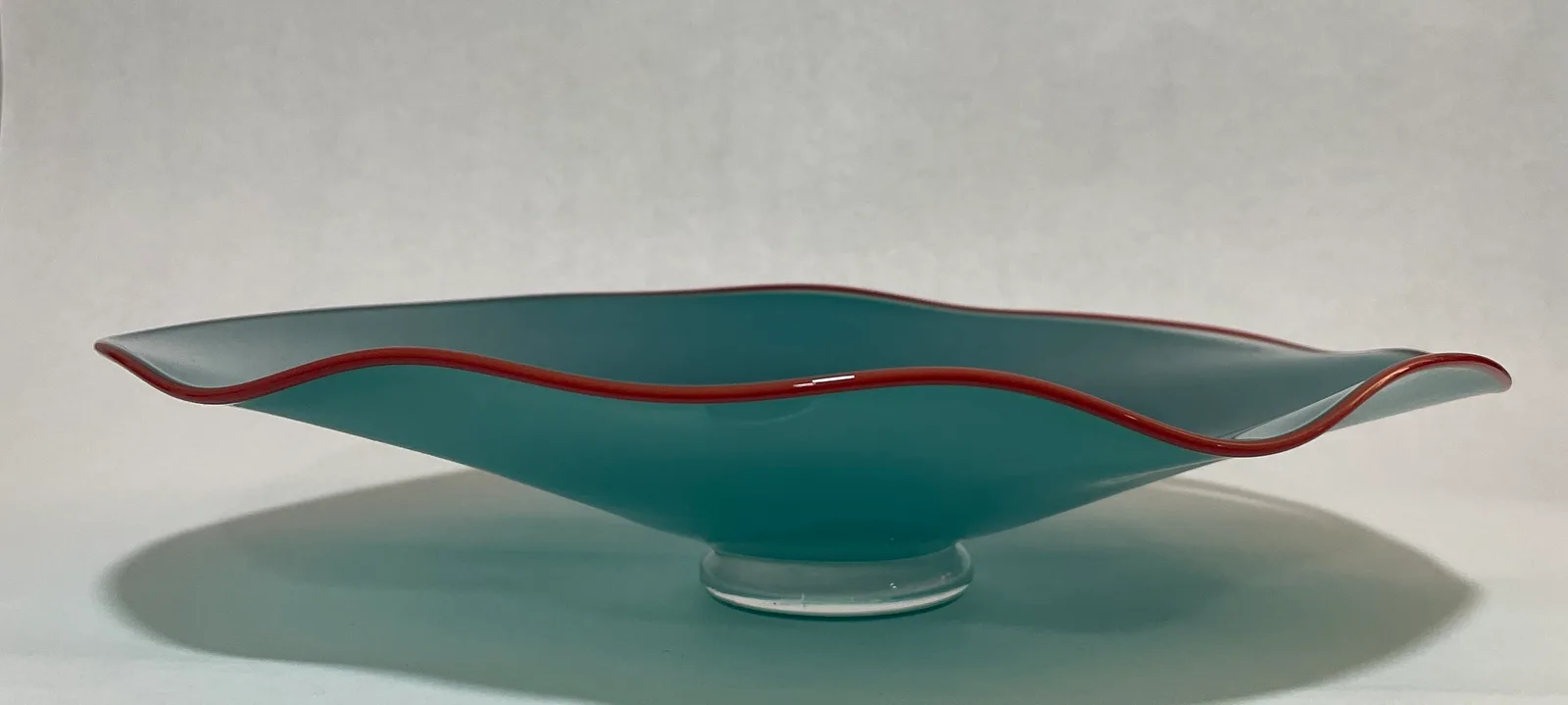 Sculptural glass vessel in turquoise with red accent rim, organic curved form.