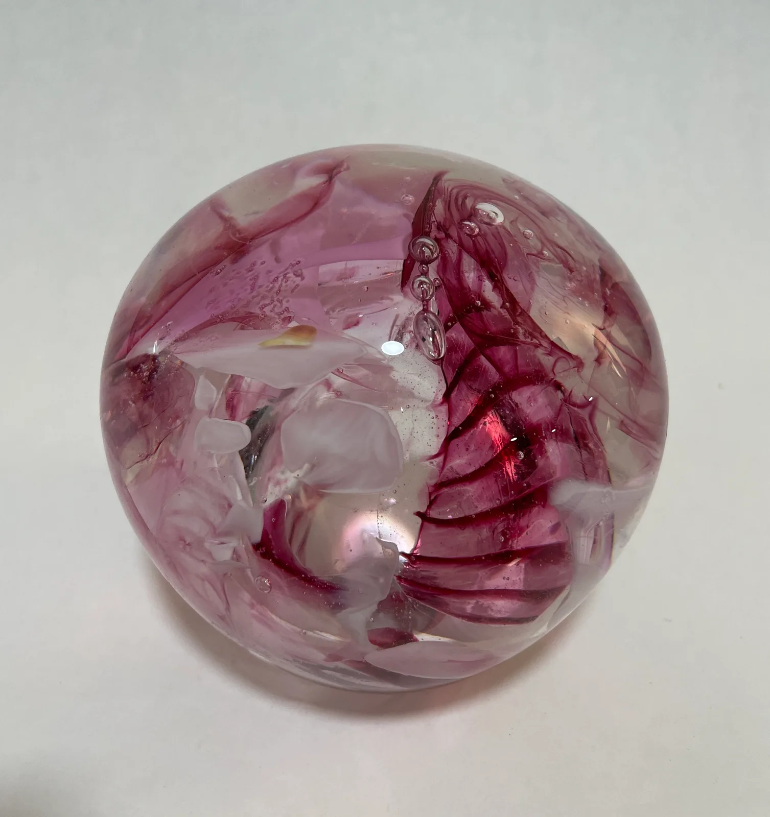A translucent spherical glass sculpture in shades of mauve and deep rose with internal carved forms.