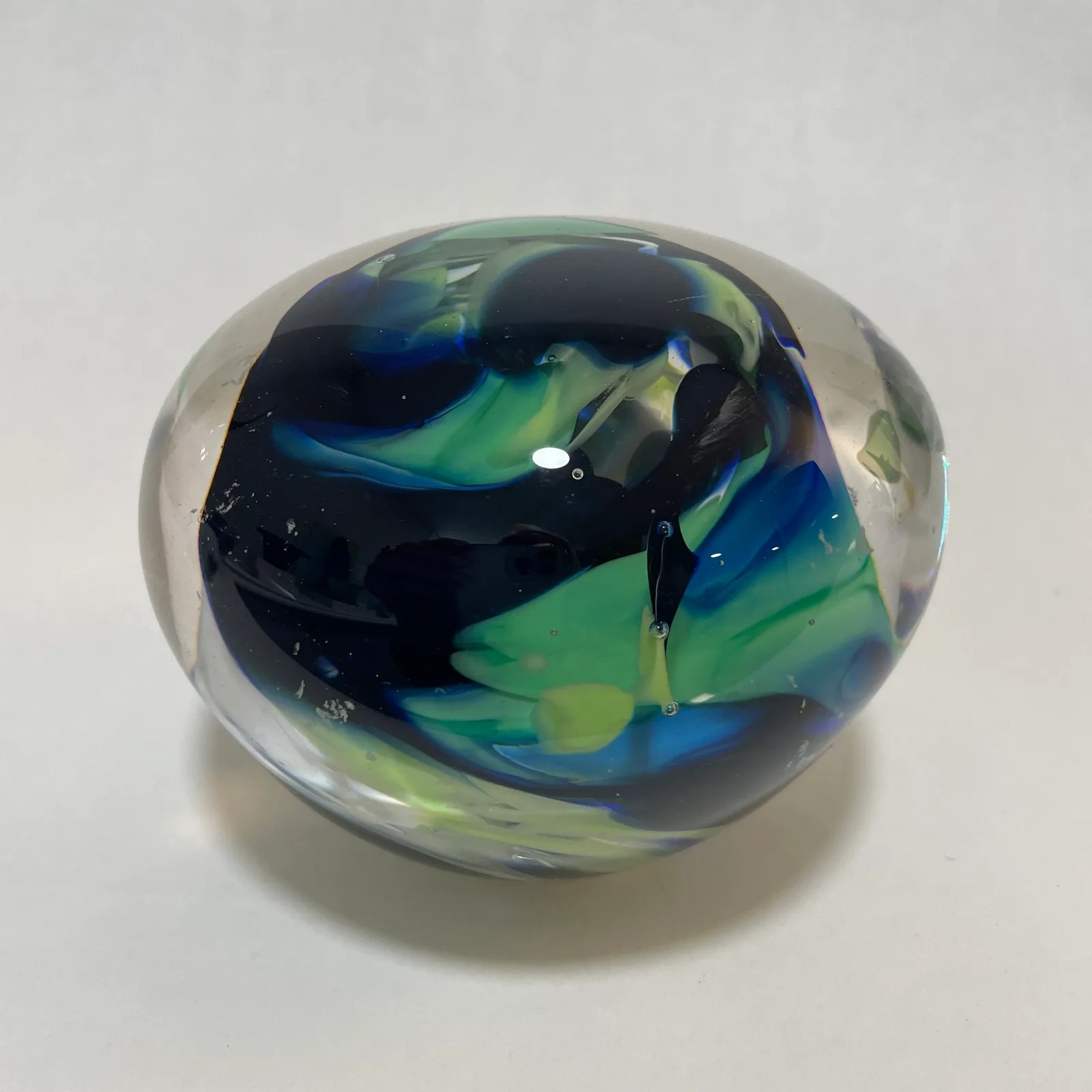 Abstract glass orb with blue, green, and black swirled interior, photographed on white background.