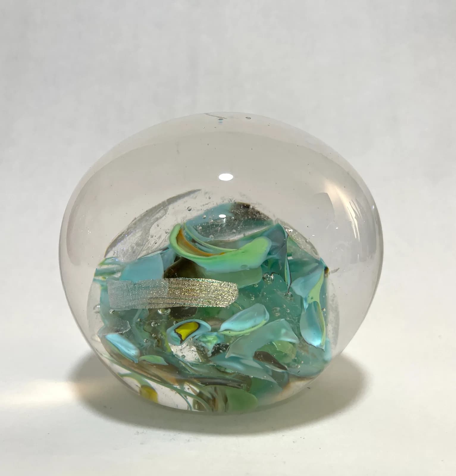 A glass sphere paperweight encases layered turquoise, gold, and aqua glass fragments in clear crystal.