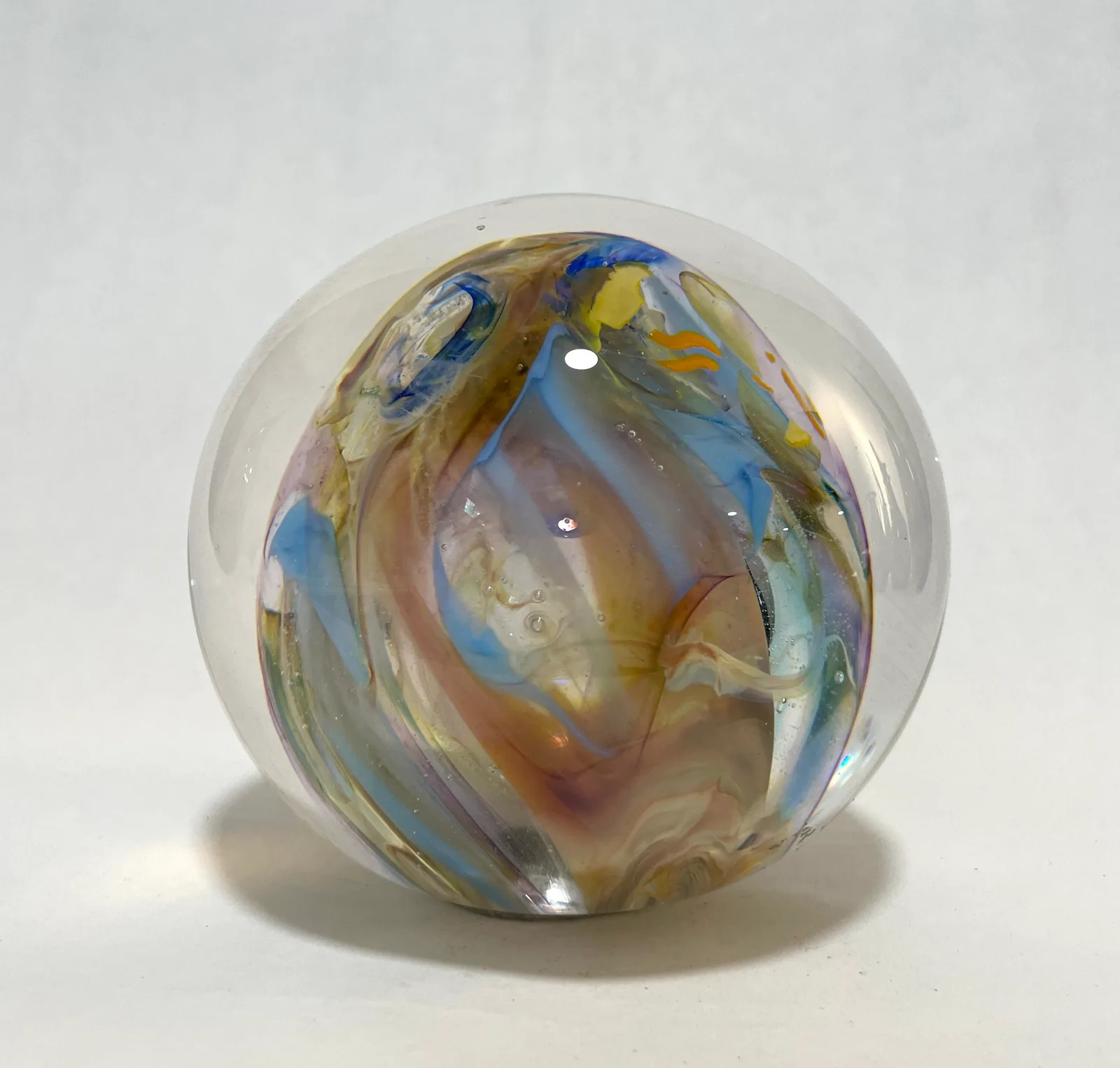 A spherical blown-glass form with swirling bands of blue, amber, and earth tones.