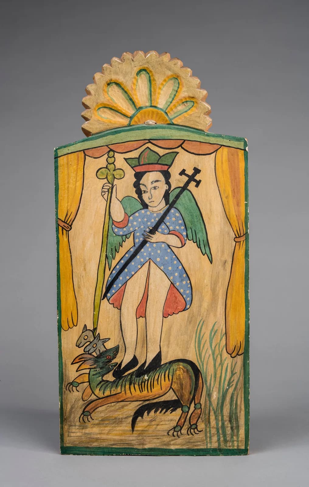 Hand-carved and painted wooden retablo depicting a winged saint figure with a demon, rendered in folk art style.