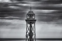 A black-and-white photograph of an isolated tower structure set against a turbulent, darkened sky.