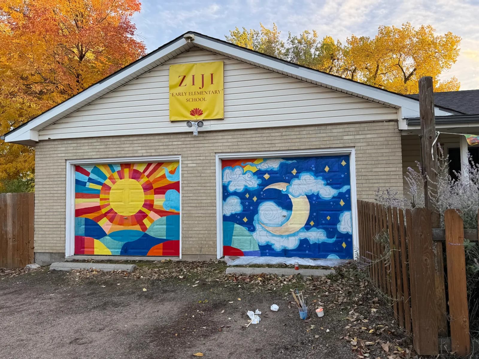 Two vibrant garage-door murals depicting a colorful sun and a blue nighttime moon with stars and clouds.