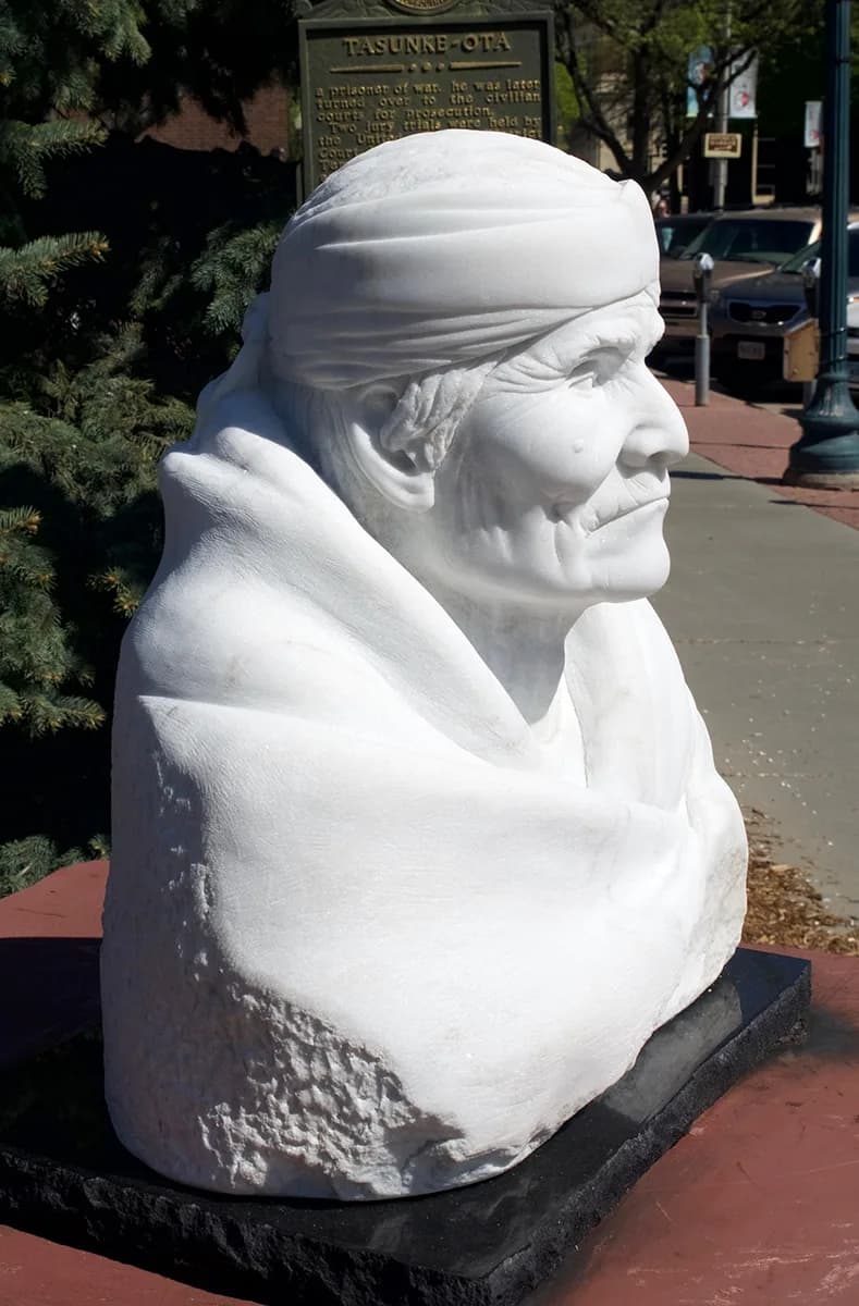 White stone portrait bust of a figure with wrapped headcloth, carved in relief.