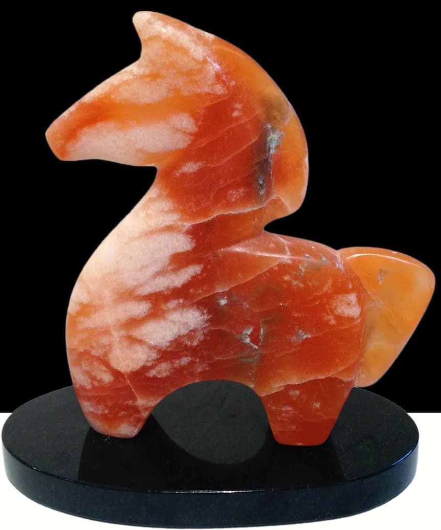 Carved stone sculpture in warm orange-red with abstract animal-like form mounted on a black base.