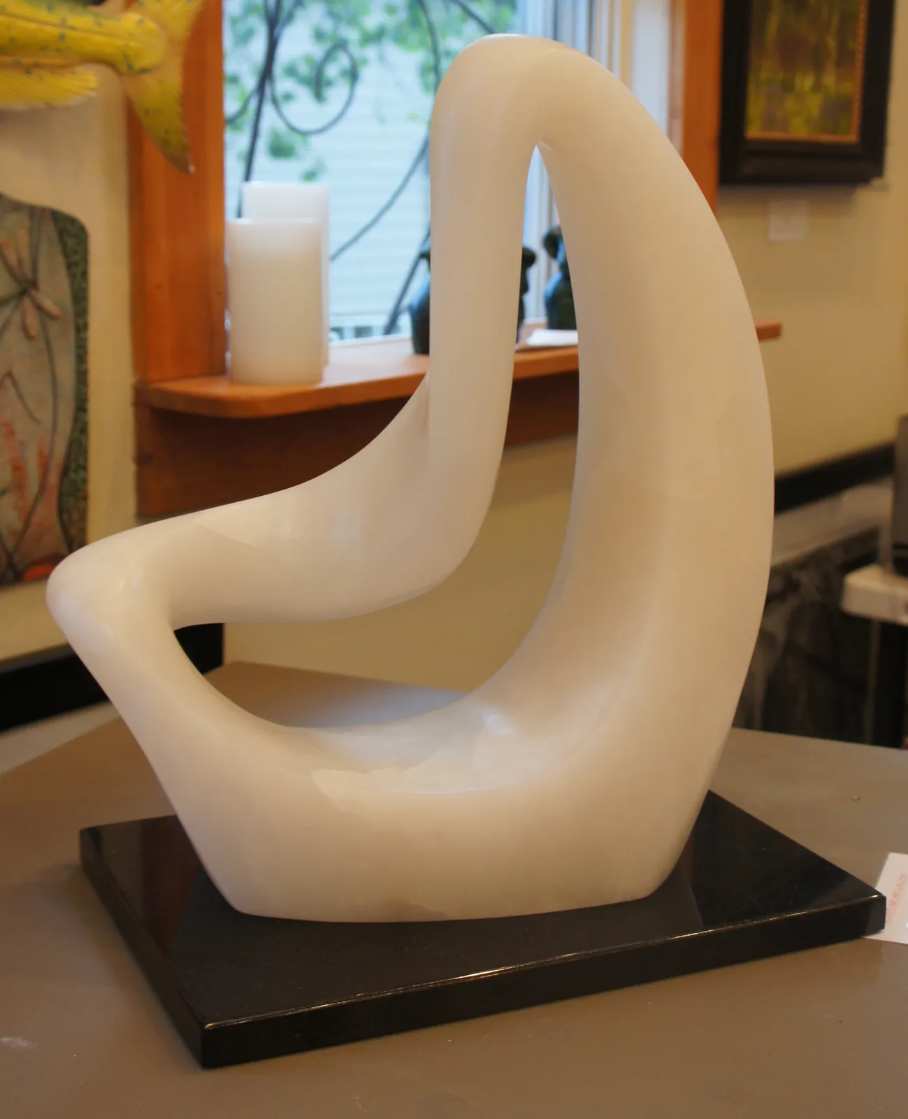 Abstract sculptural form in cream-colored material with interlocking curved loops on a black base.