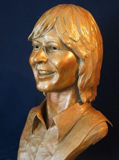 Carved wooden portrait bust of a woman with glasses and shoulder-length hair.