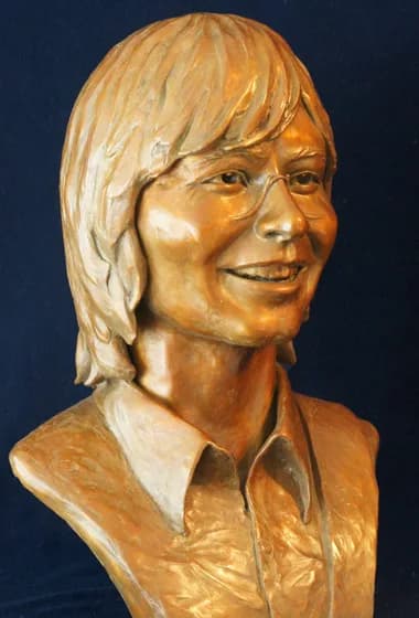 Bronze portrait bust of a man with long hair, rendered in warm golden tones against a dark background.