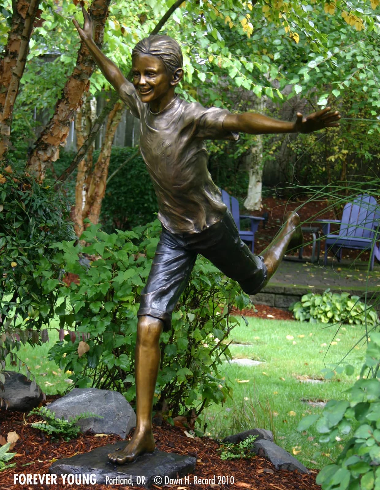 Bronze figurative sculpture of a joyful young figure in a garden setting.