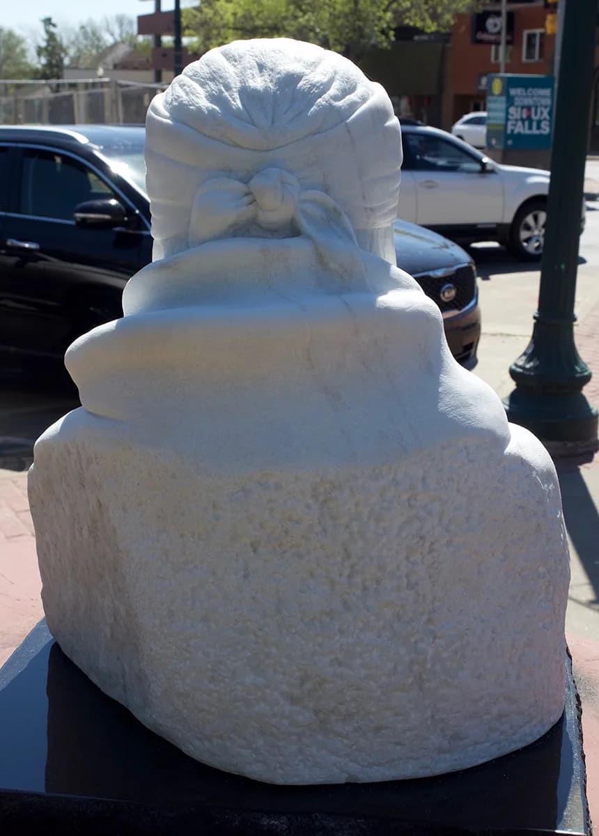 Abstract carved stone sculpture with stacked rounded and geometric forms, displayed in an urban plaza.
