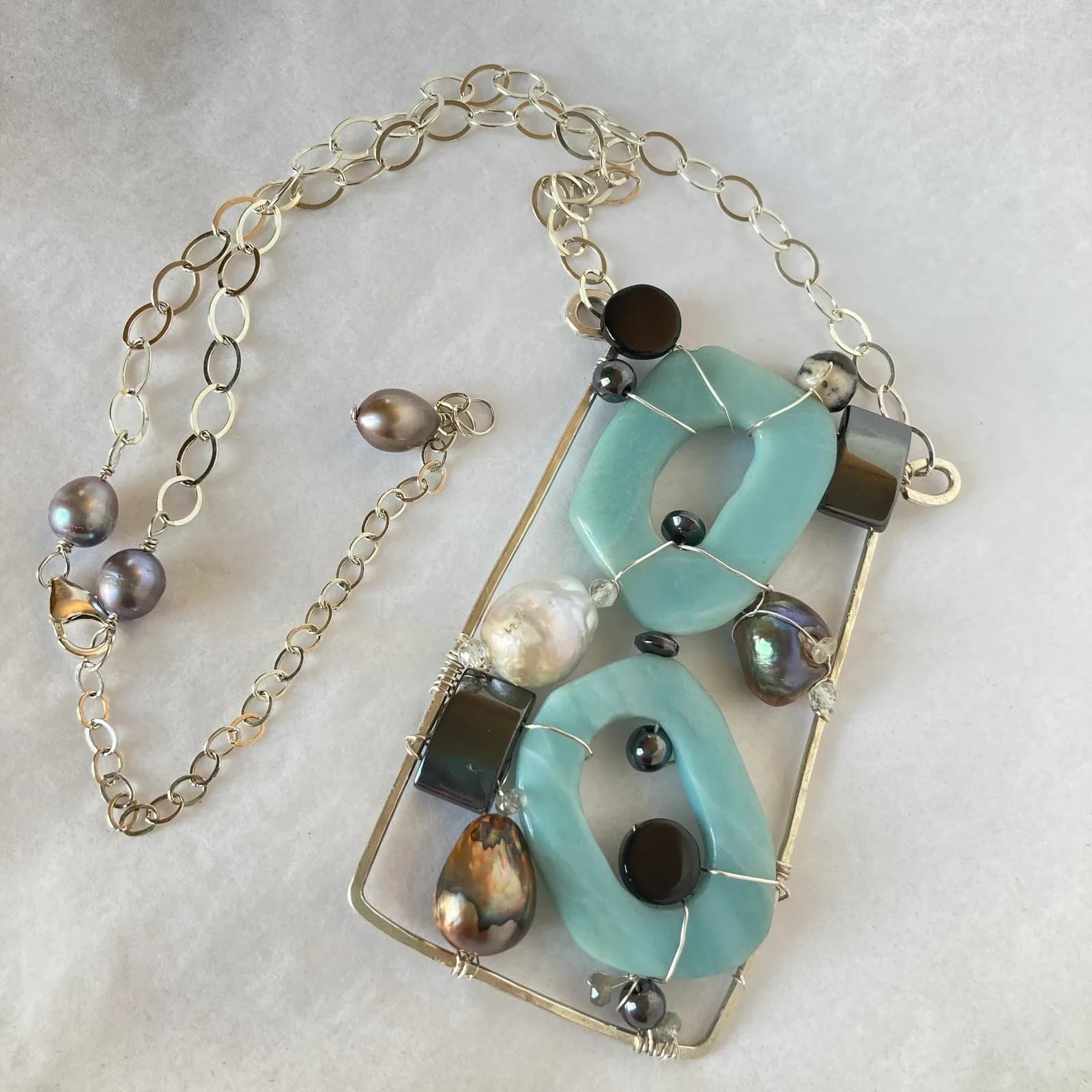 Mixed-metal and turquoise pendant necklace with pearls, onyx, and geometric wire framing on silver chain.