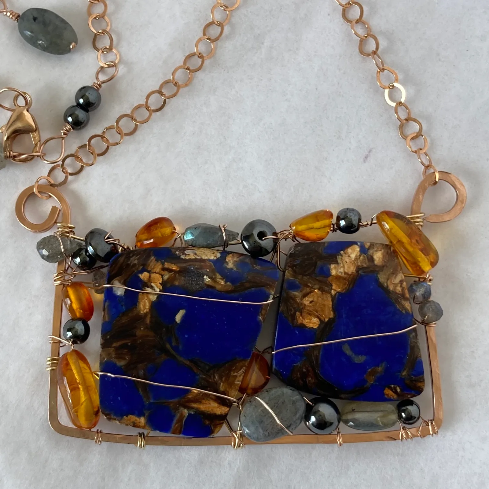 Wire-wrapped pendant necklace with lapis, amber, and hematite beads suspended from a copper chain.